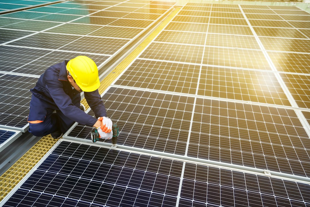 Instalator care montează panouri fotovoltaice pe acoperișul unei case